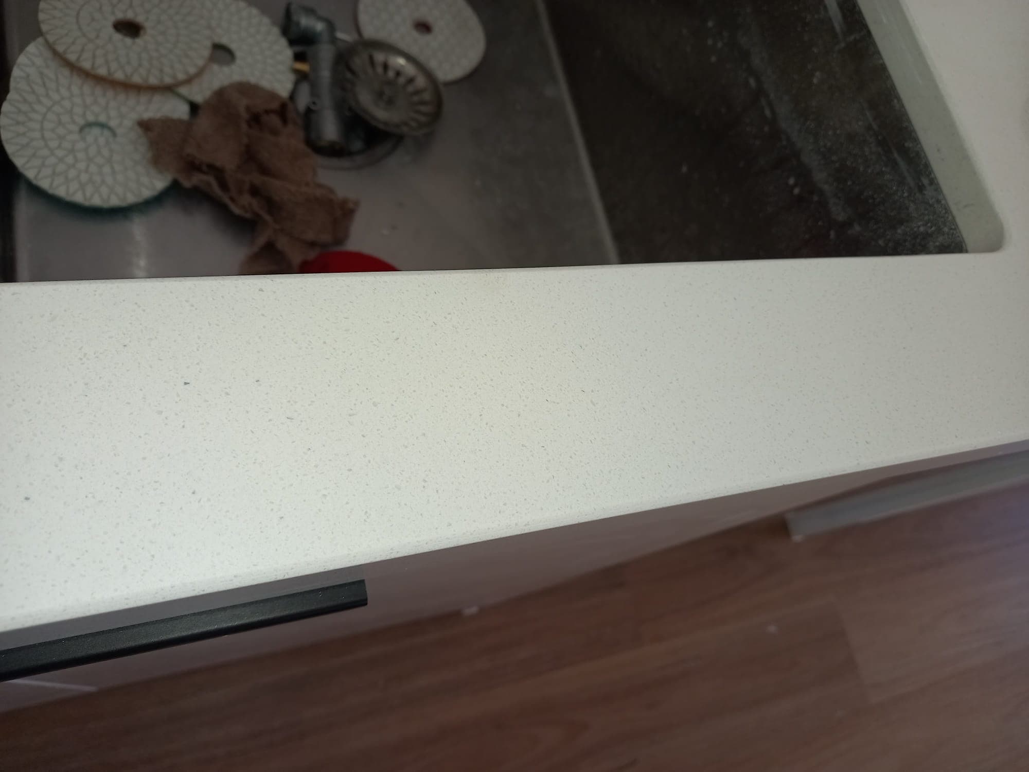 After: the white stone benchtop edge by the sink with the chip filled and polished smooth.
